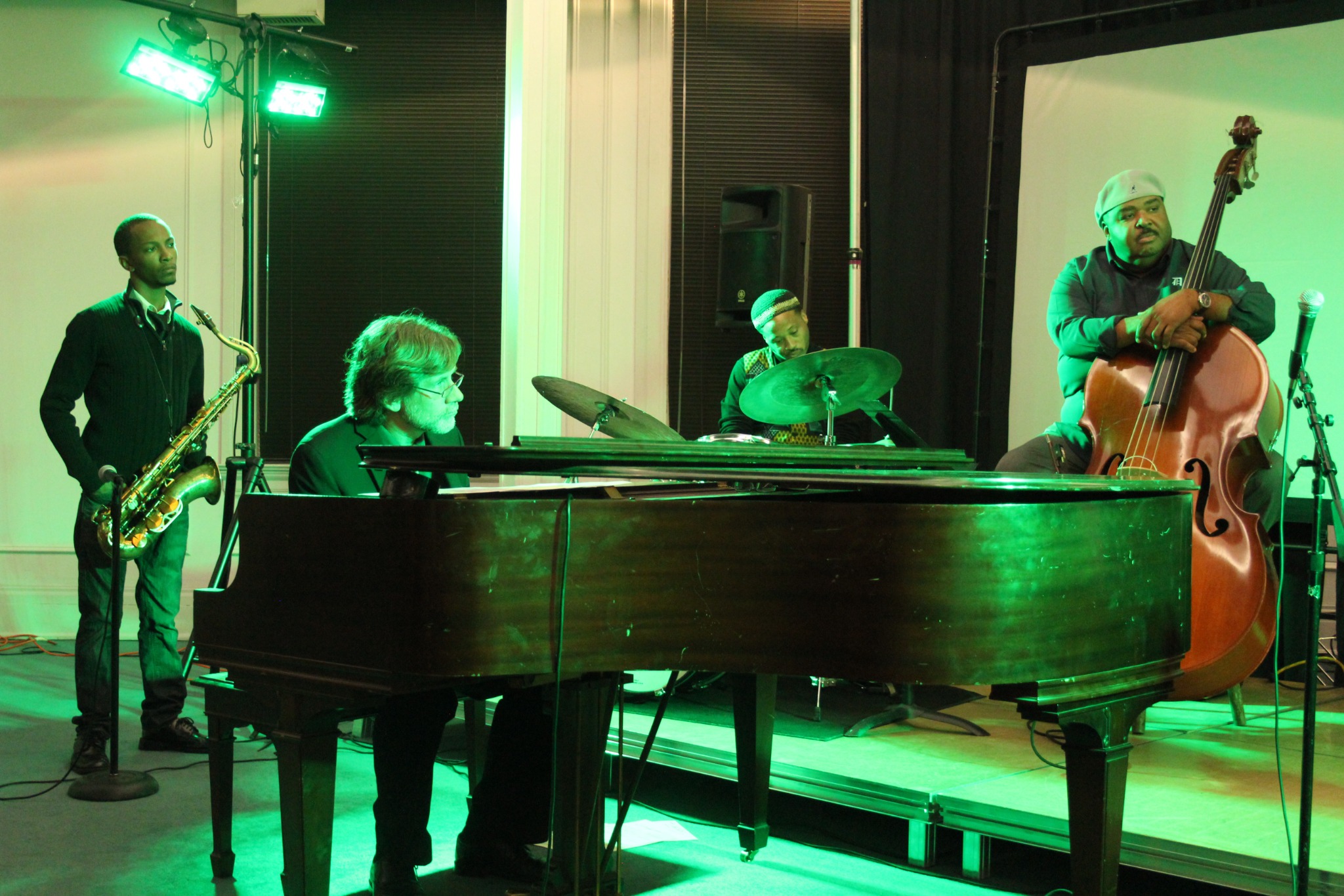 Jazz ensemble performing under green stage lighting with saxophone, piano, drums, and upright bass